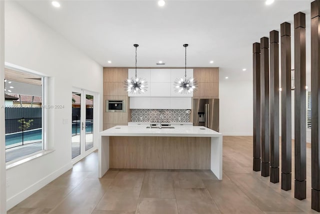 kitchen with white cabinets, stainless steel appliances, sink, decorative backsplash, and a center island with sink