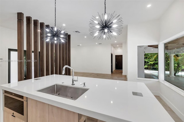 kitchen with an inviting chandelier, decorative light fixtures, sink, light brown cabinets, and a center island with sink