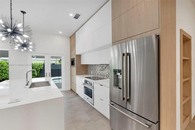 kitchen with hanging light fixtures, appliances with stainless steel finishes, white cabinetry, sink, and tasteful backsplash