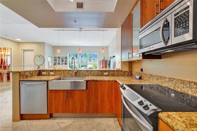 kitchen featuring light stone counters, stainless steel appliances, sink, kitchen peninsula, and decorative light fixtures