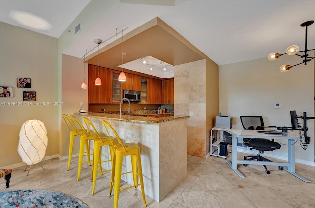 kitchen featuring an inviting chandelier, a kitchen breakfast bar, decorative light fixtures, light stone counters, and kitchen peninsula