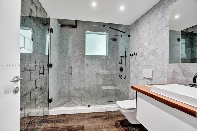 bathroom with toilet, a shower with door, vanity, wood-type flooring, and tile walls