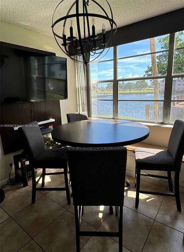 dining space featuring a chandelier, a textured ceiling, a water view, and dark tile patterned floors