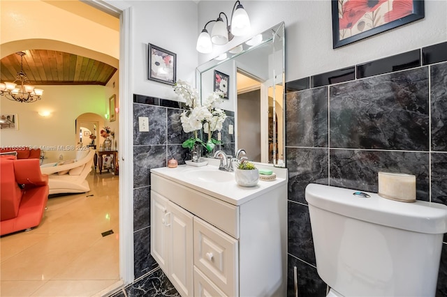 bathroom with an inviting chandelier, wooden ceiling, toilet, tile walls, and vanity