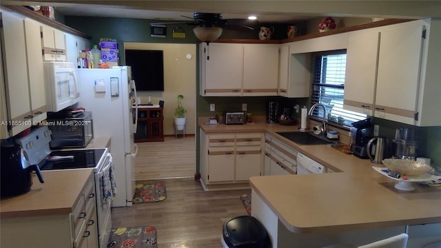 kitchen featuring white appliances, wood finished floors, light countertops, and a sink