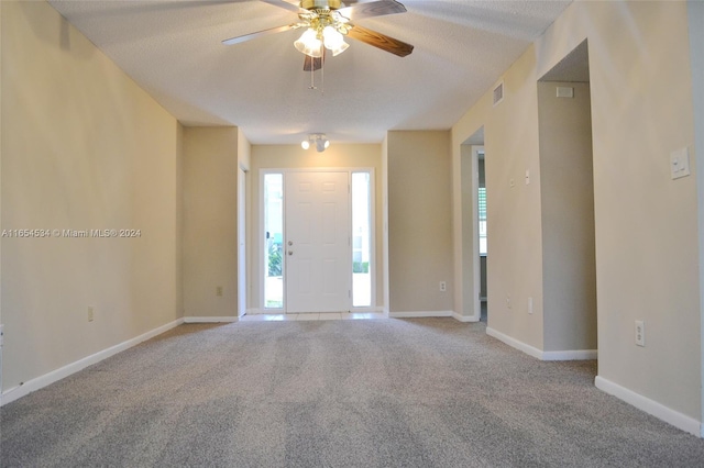 foyer entrance with ceiling fan, light carpet, and a textured ceiling