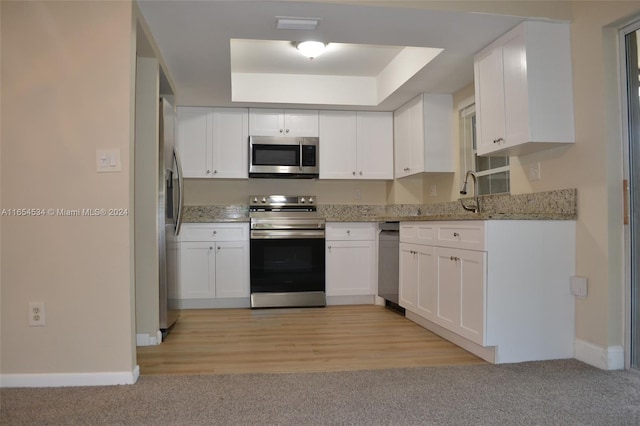 kitchen featuring white cabinets, appliances with stainless steel finishes, light stone counters, and light hardwood / wood-style floors