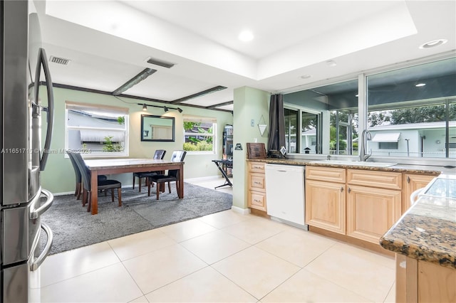 kitchen with dark stone counters, stainless steel fridge, light tile patterned floors, white dishwasher, and light brown cabinets