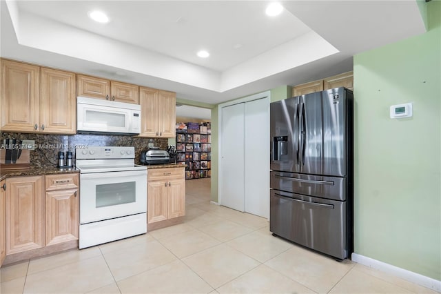 kitchen with a tray ceiling, white appliances, light brown cabinetry, and light tile patterned floors