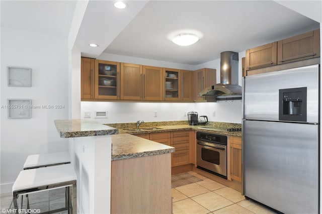 kitchen featuring dark stone countertops, appliances with stainless steel finishes, sink, wall chimney exhaust hood, and kitchen peninsula