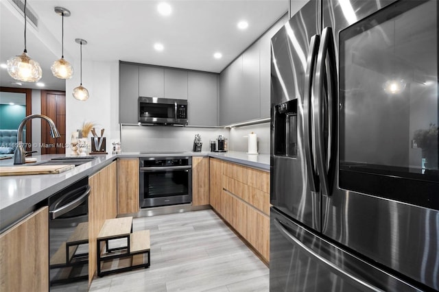 kitchen featuring light wood-type flooring, gray cabinets, stainless steel appliances, decorative light fixtures, and sink