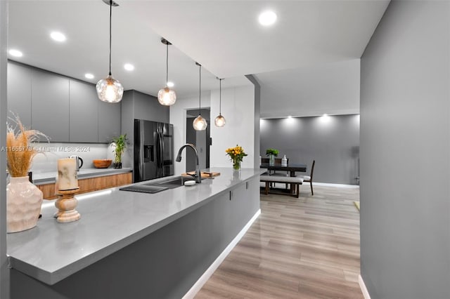 kitchen with gray cabinetry, pendant lighting, refrigerator with ice dispenser, sink, and light wood-type flooring