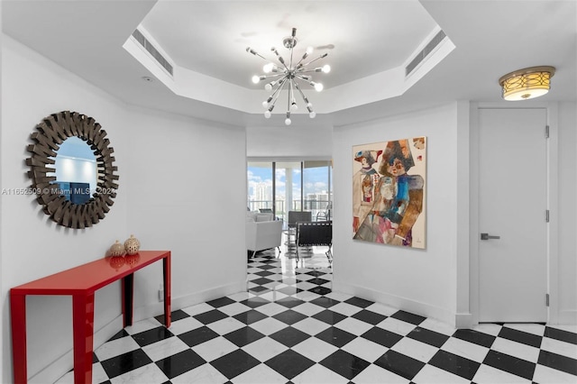 hallway with a raised ceiling and a notable chandelier