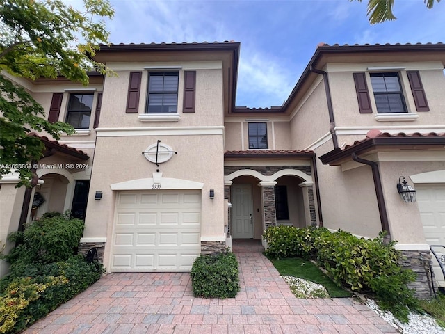 view of front of property featuring an attached garage, stucco siding, stone siding, a tiled roof, and decorative driveway