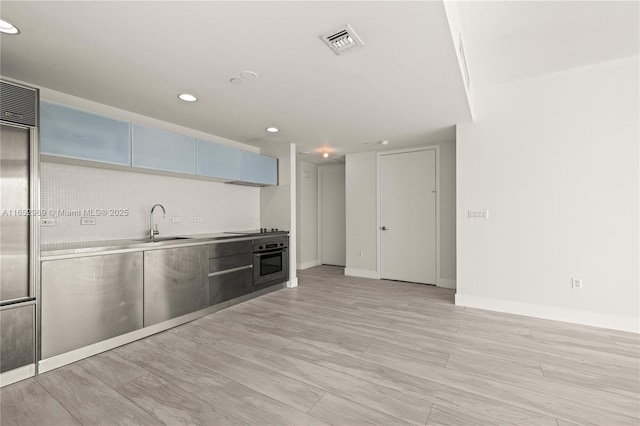 kitchen featuring stainless steel counters, sink, oven, and light wood-type flooring