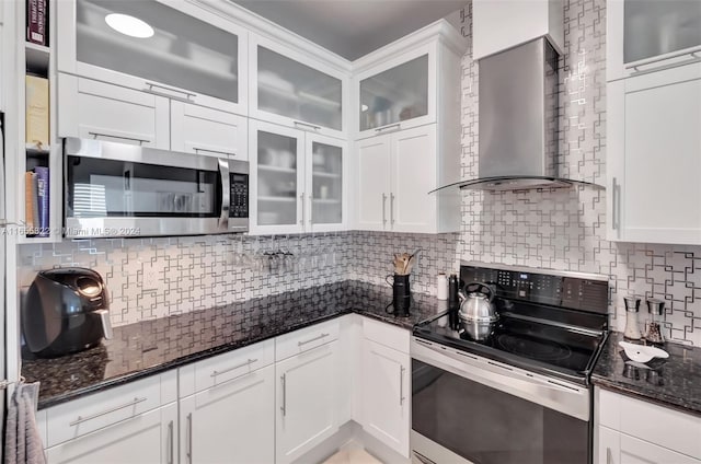 kitchen featuring white cabinets, stainless steel appliances, wall chimney range hood, dark stone counters, and tasteful backsplash