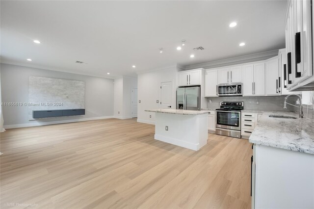 kitchen with light hardwood / wood-style flooring, light stone counters, a center island, sink, and appliances with stainless steel finishes