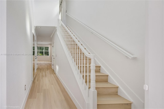 staircase featuring baseboards, a high ceiling, and wood finished floors