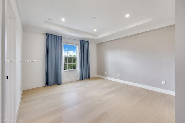 empty room with recessed lighting, baseboards, a raised ceiling, and light wood-style flooring