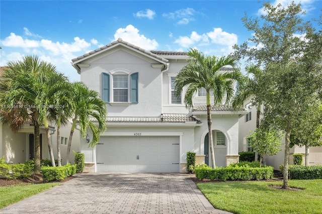 mediterranean / spanish house featuring a tiled roof, decorative driveway, an attached garage, and stucco siding