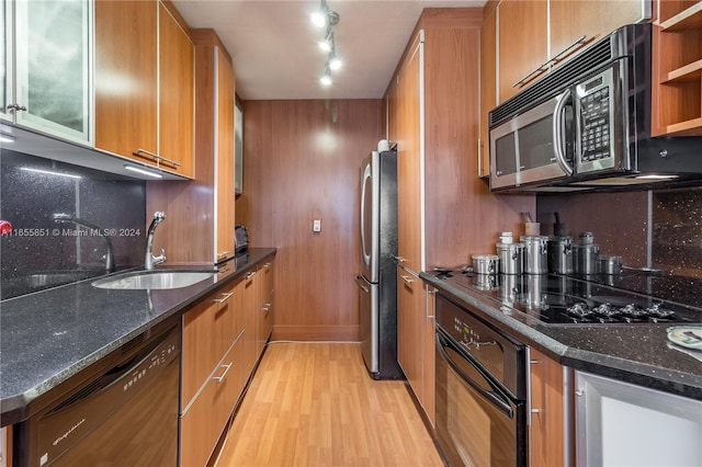 kitchen with black appliances, backsplash, sink, light wood-type flooring, and dark stone counters