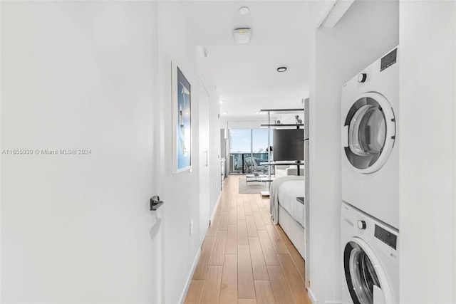 clothes washing area with light wood-type flooring, baseboards, stacked washer and dryer, and laundry area