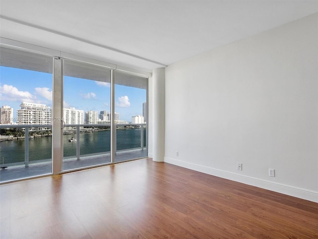 spare room with a water view, a wall of windows, and wood-type flooring