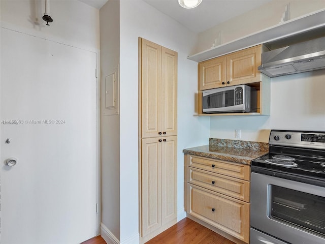 kitchen featuring dark stone countertops, wood-type flooring, light brown cabinets, appliances with stainless steel finishes, and extractor fan