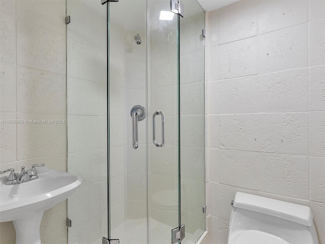 bathroom featuring a shower with shower door, toilet, and sink