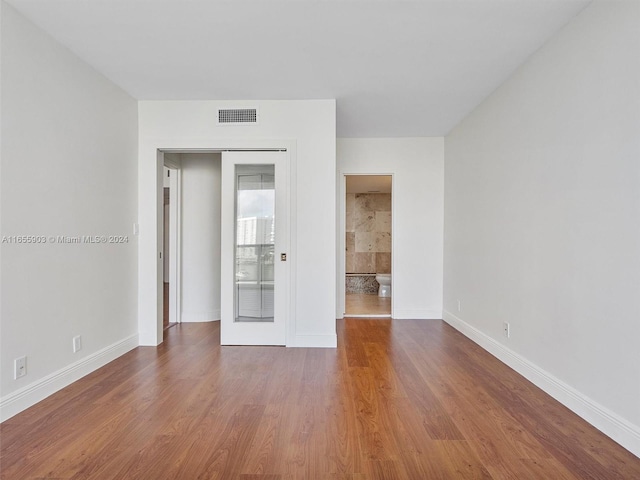 unfurnished bedroom with connected bathroom and hardwood / wood-style flooring