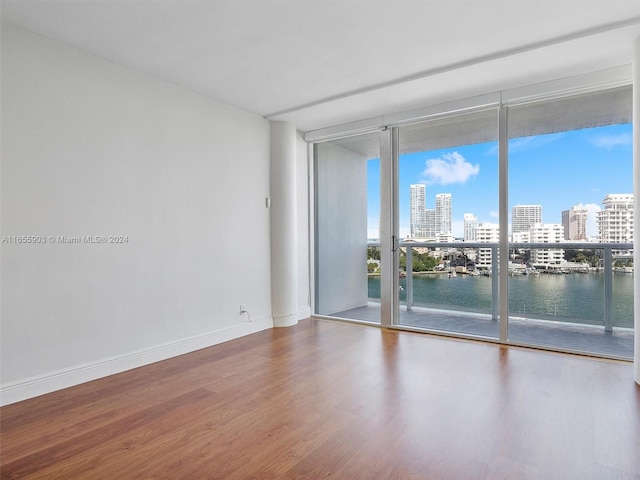 spare room with hardwood / wood-style flooring, a water view, and a wall of windows