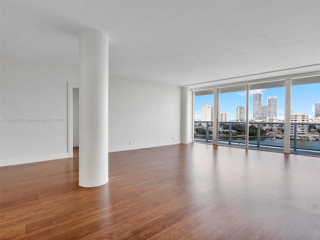 empty room with a wealth of natural light, floor to ceiling windows, and dark hardwood / wood-style floors