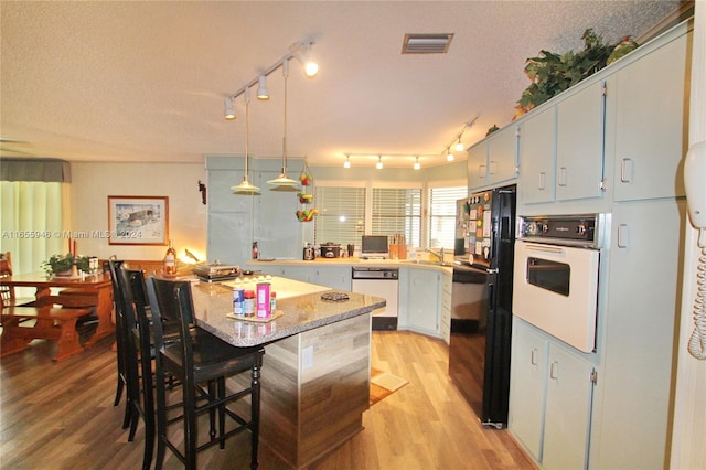 kitchen featuring a textured ceiling, light hardwood / wood-style flooring, oven, dishwashing machine, and black refrigerator