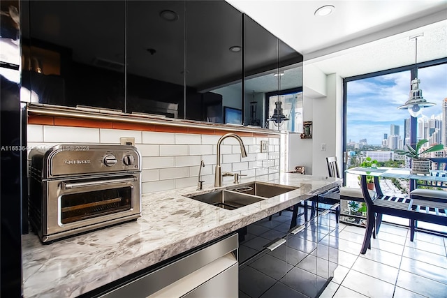 kitchen featuring backsplash, dishwasher, light stone counters, sink, and hanging light fixtures