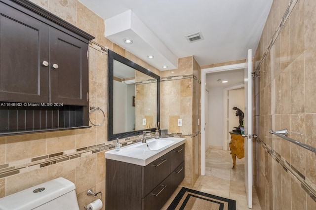 bathroom with vanity, toilet, a tile shower, tile walls, and tile patterned flooring