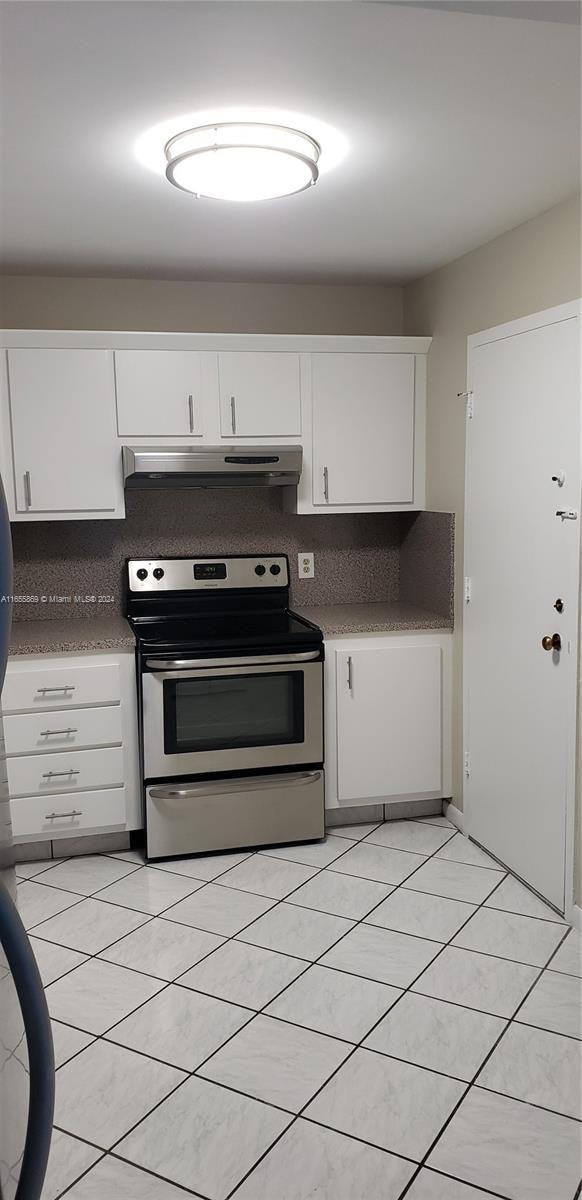 kitchen featuring light tile patterned floors, stainless steel electric stove, and white cabinetry