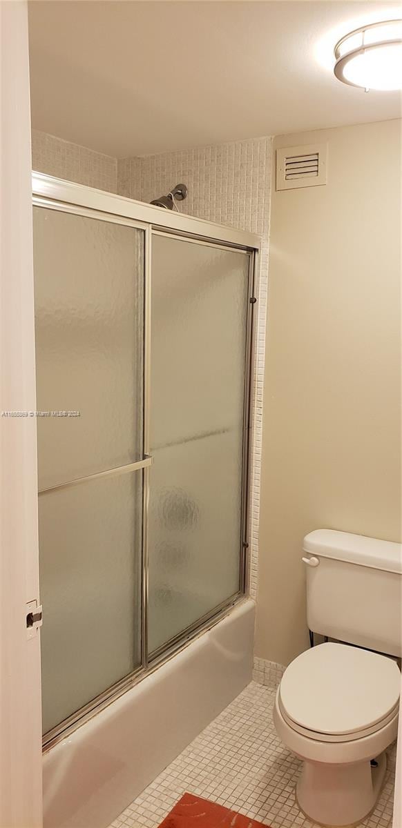 bathroom featuring combined bath / shower with glass door, toilet, and tile patterned floors