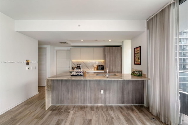 kitchen featuring kitchen peninsula, light wood-type flooring, tasteful backsplash, and sink