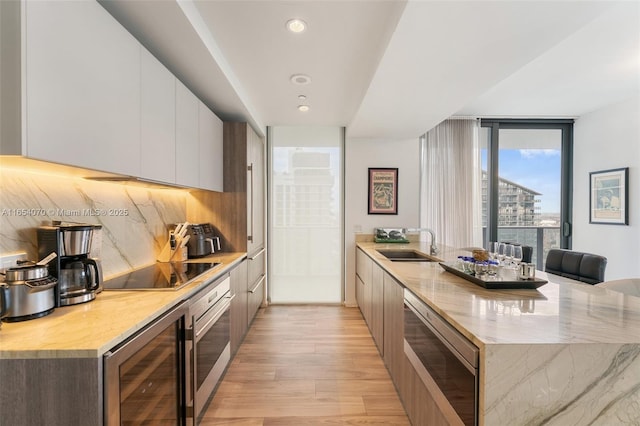 kitchen with appliances with stainless steel finishes, white cabinetry, wine cooler, sink, and floor to ceiling windows