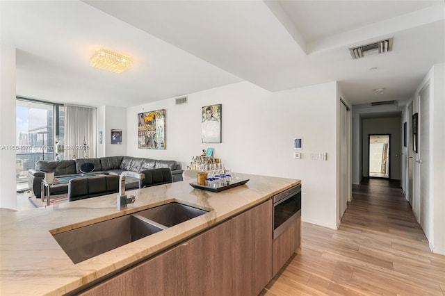 kitchen featuring stainless steel microwave, light stone countertops, light hardwood / wood-style floors, a wall of windows, and sink