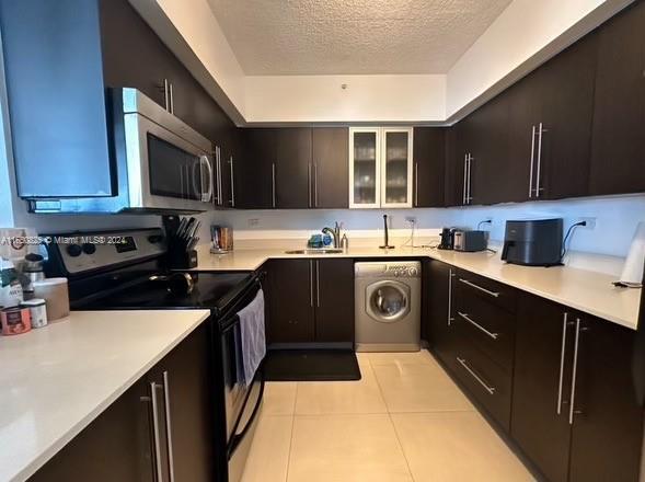 kitchen featuring appliances with stainless steel finishes, washer / clothes dryer, light tile patterned floors, a textured ceiling, and sink