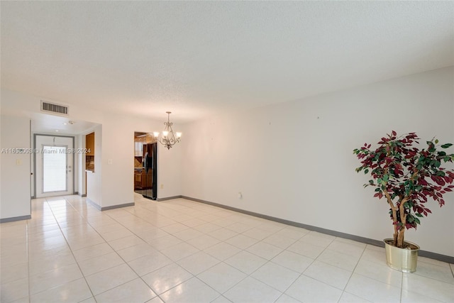 tiled empty room featuring a notable chandelier and a textured ceiling