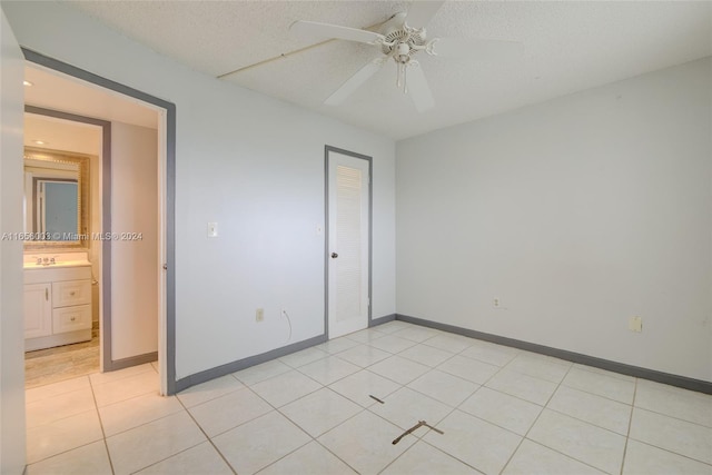 unfurnished bedroom featuring ceiling fan, a closet, sink, light tile patterned floors, and a textured ceiling