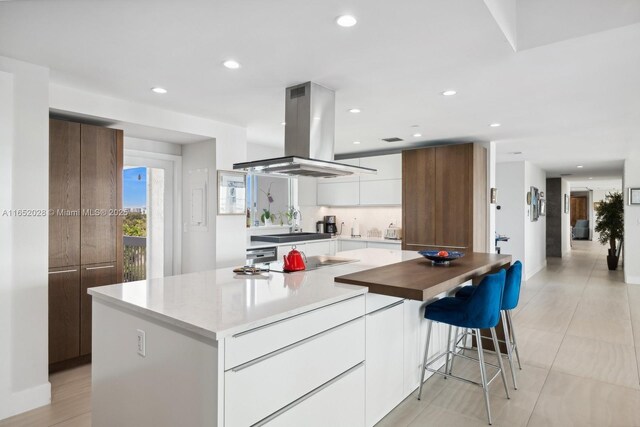 kitchen featuring sink, island range hood, black electric cooktop, a kitchen island, and white cabinets