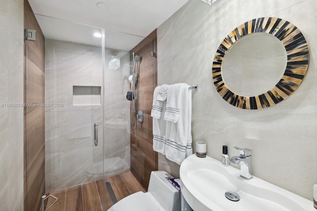 bathroom featuring tile walls, sink, a shower with door, and toilet