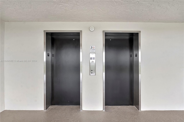 corridor featuring light colored carpet, a textured ceiling, and elevator