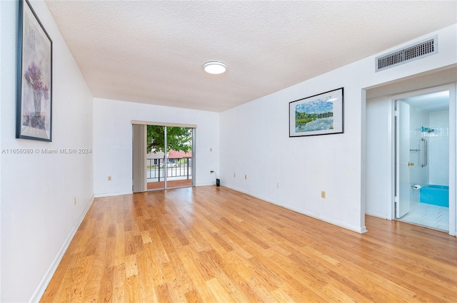 unfurnished room with light wood-type flooring and a textured ceiling