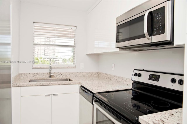 kitchen featuring appliances with stainless steel finishes, light stone counters, white cabinetry, and sink