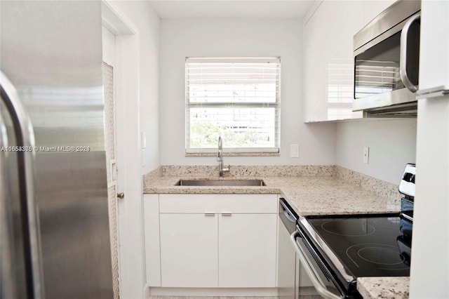 kitchen with appliances with stainless steel finishes, light stone countertops, white cabinetry, and sink