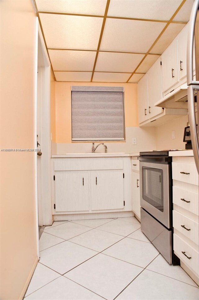 kitchen with a paneled ceiling, light tile patterned floors, sink, stainless steel range oven, and white cabinets